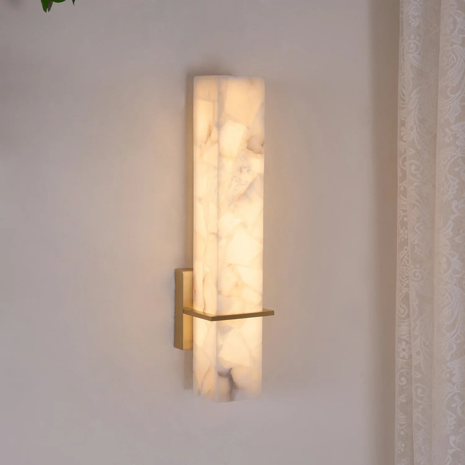 Alabaster cuboid wall light lit at an angle on a pale wall, brass crossbar catching the glow