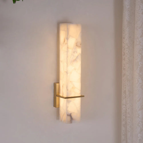 Alabaster cuboid wall light lit at an angle on a pale wall, brass crossbar catching the glow