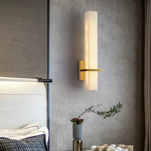 Alabaster wall light lit beside a white leather headboard on a grey plaster bedroom wall