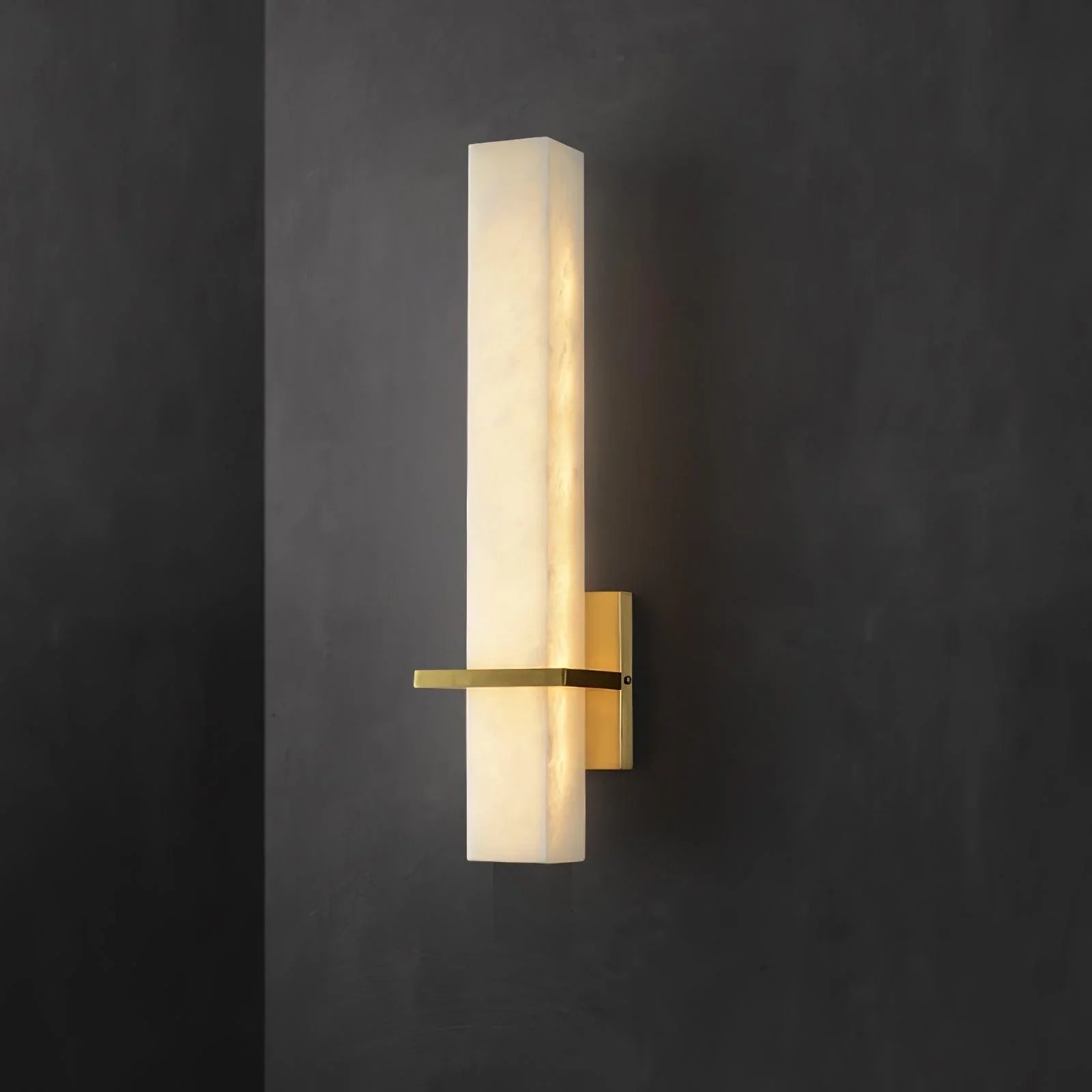 Alabaster wall light lit against a dark charcoal wall, brass arm extending to the left