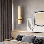 The wall light lit above a bed ledge, framed prints leaning against the raw concrete wall