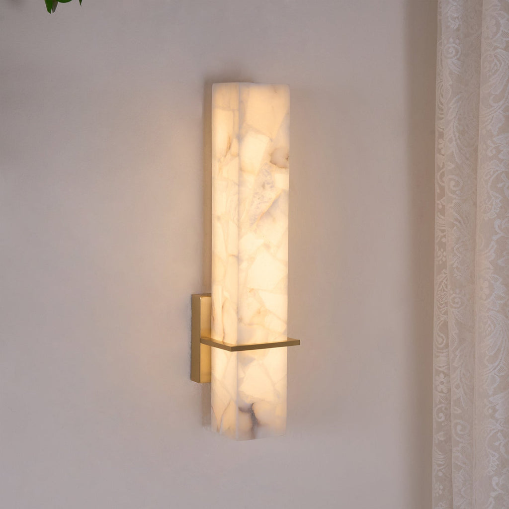 Close angled view of the lit fixture, warm light washing the cream wall behind the alabaster