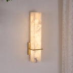 Close angled view of the lit fixture, warm light washing the cream wall behind the alabaster