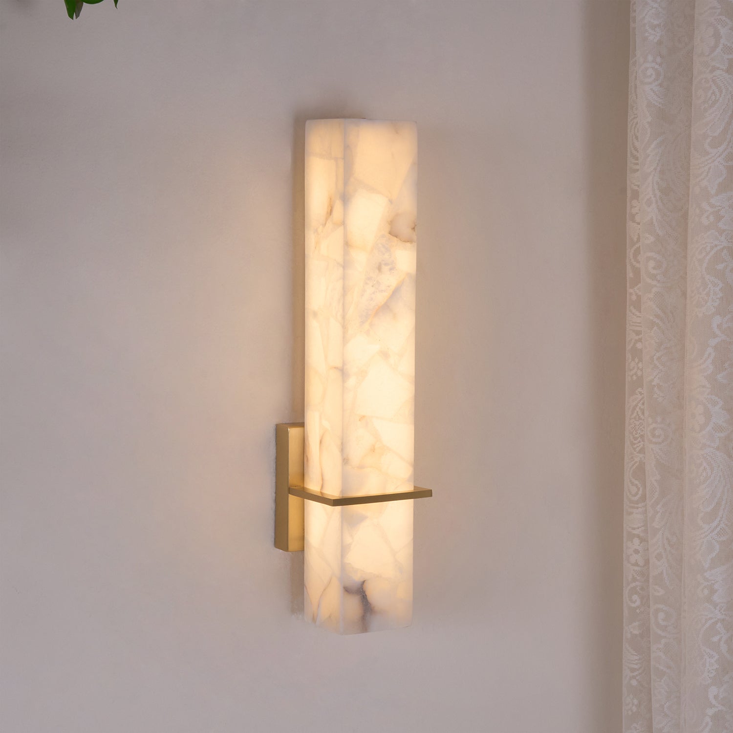 Close angled view of the lit fixture, warm light washing the cream wall behind the alabaster