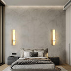 Wide bedroom view with a pair of alabaster wall lights lit either side of a grey upholstered bed
