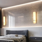 Two alabaster wall lights lit on a textured wall above a bed, reflected in the long mirror behind