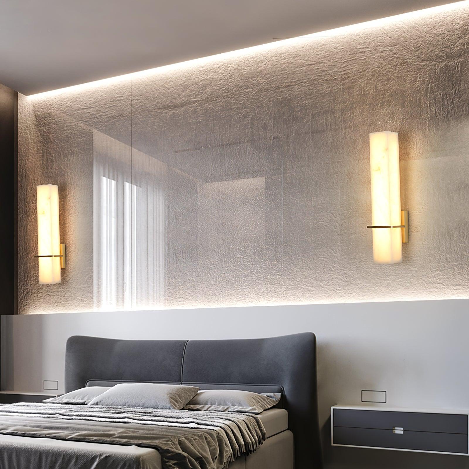 Two alabaster wall lights lit on a textured wall above a bed, reflected in the long mirror behind