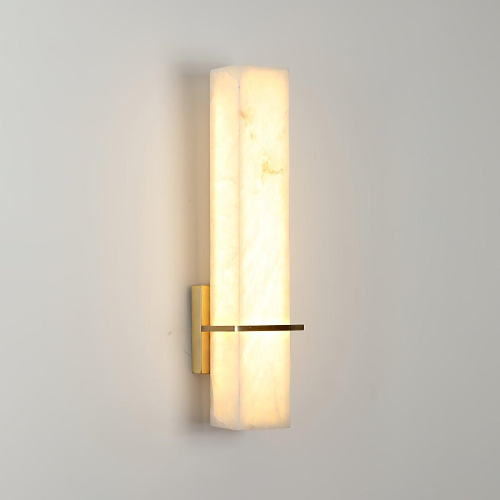 Single wall light lit on a plain grey wall, alabaster glowing warm around the brass bar