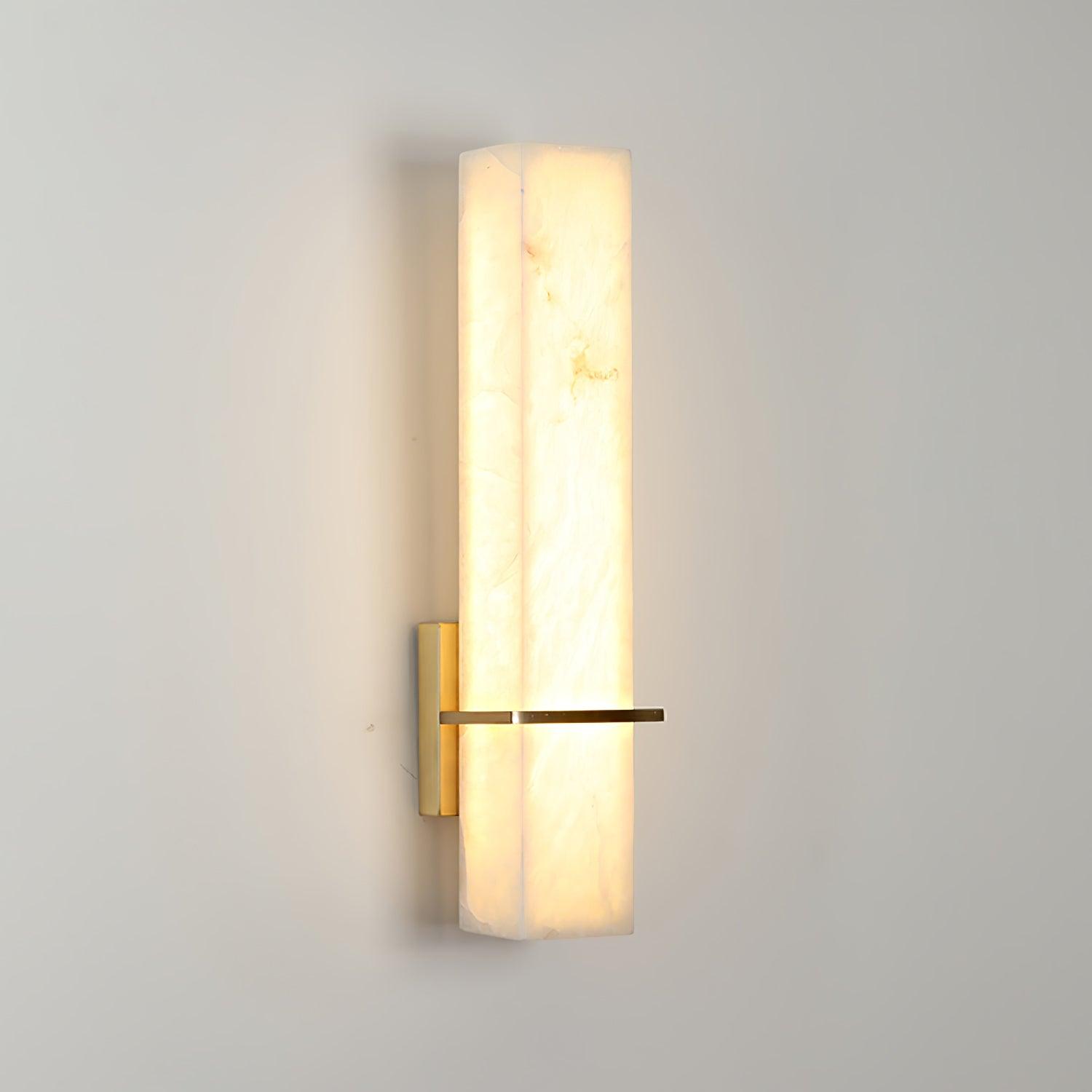 Single wall light lit on a plain grey wall, alabaster glowing warm around the brass bar