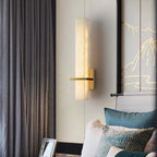 Alabaster wall light lit beside grey drapes, brass arm pointing left over teal cushioned seating