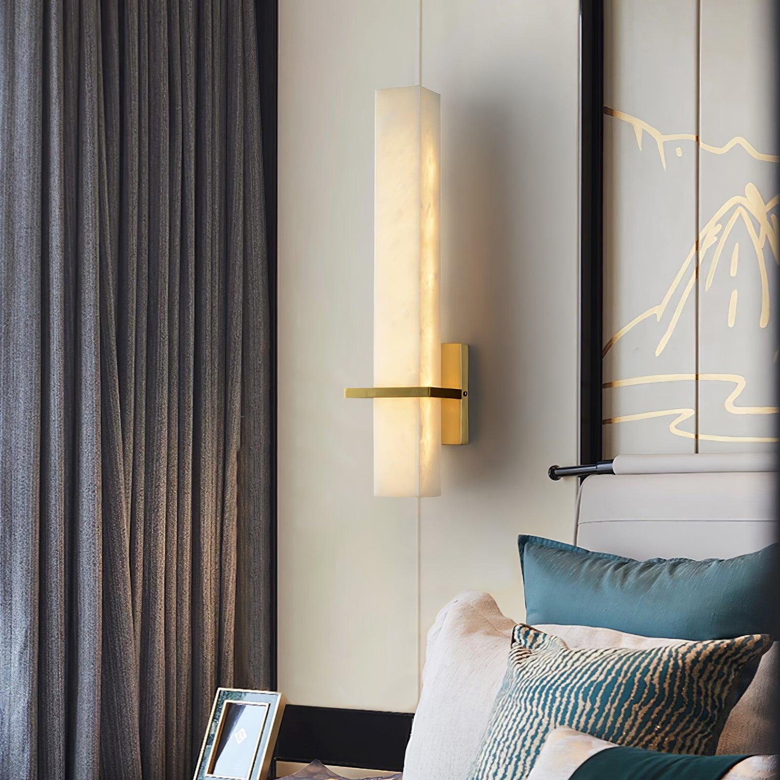 Alabaster wall light lit beside grey drapes, brass arm pointing left over teal cushioned seating