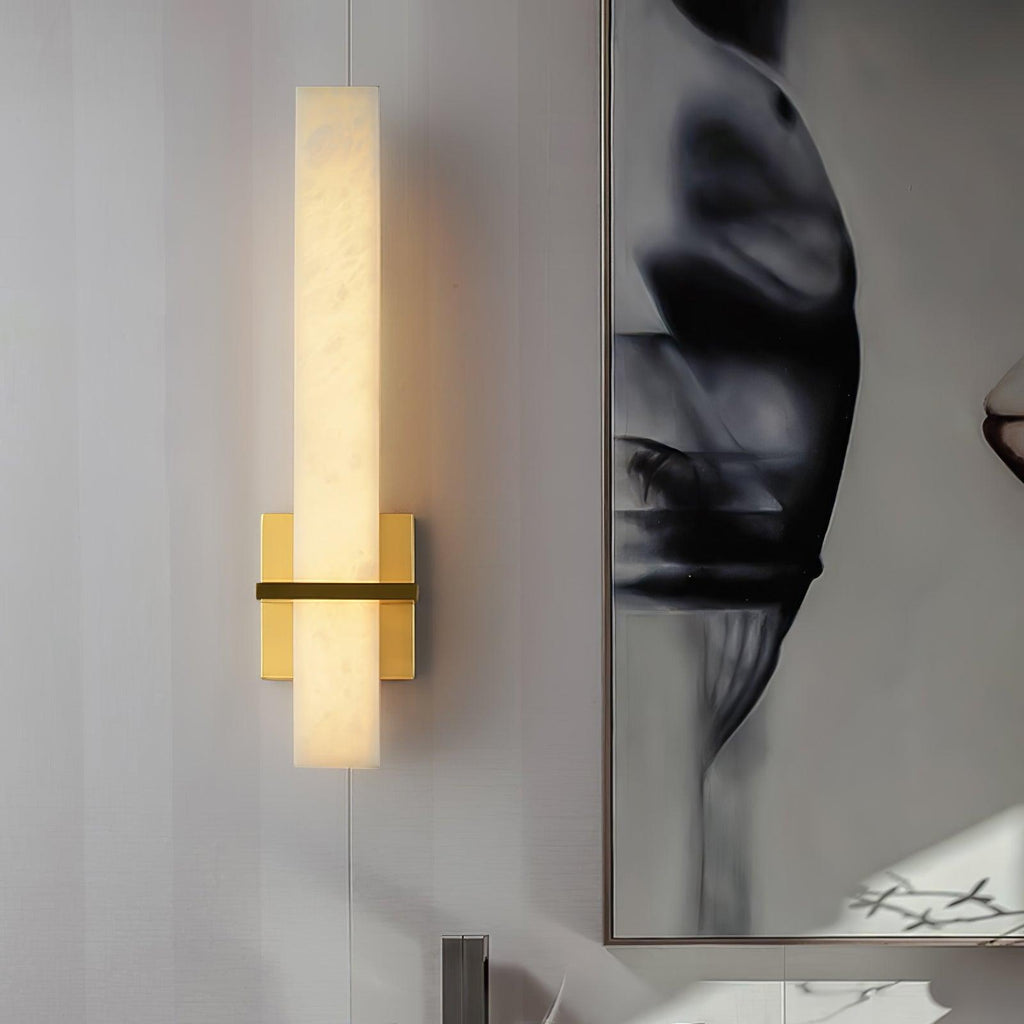 The lit wall light with polished gold backplate beside a large framed black-and-white artwork