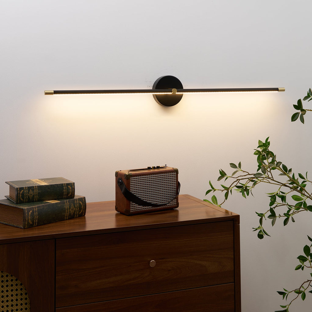 Slim linear wall lamp in gold above a dressing mirror