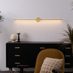 Gold linear wall lamp mounted along the top of a mirror