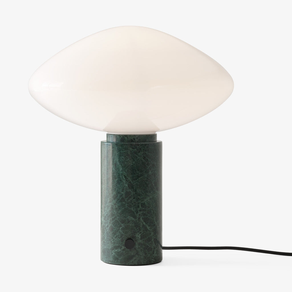 Clérachic green marble table lamp lit against a pale backdrop, framed closer than the studio shot to show its glow.