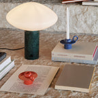 Clérachic table lamp lit on a textured stone surface beside stacked books and a blue candle holder.