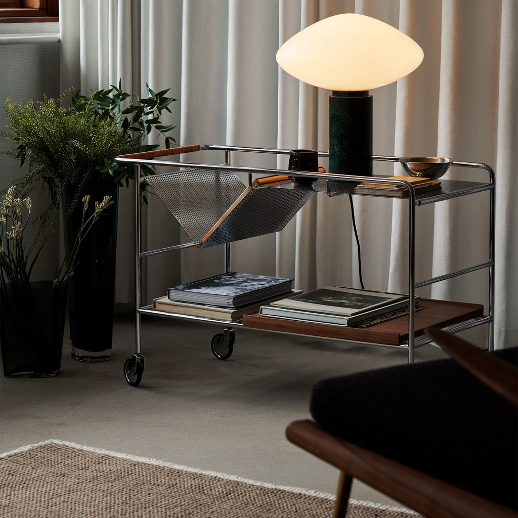 Clérachic marble table lamp lit on a wire bar cart beside a potted plant, curtains and a wheeled frame visible.