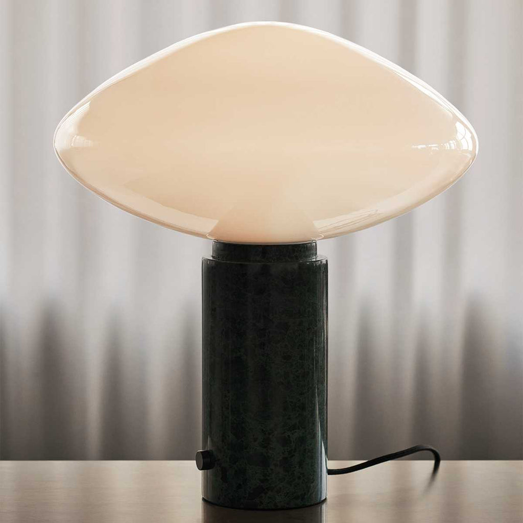 Clérachic table lamp lit on a wood surface against curtains, cropped tighter on the marble column than the matching shot.