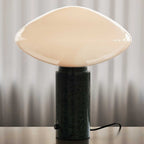 Clérachic table lamp lit on a wood surface against curtains, cropped tighter on the marble column than the matching shot.
