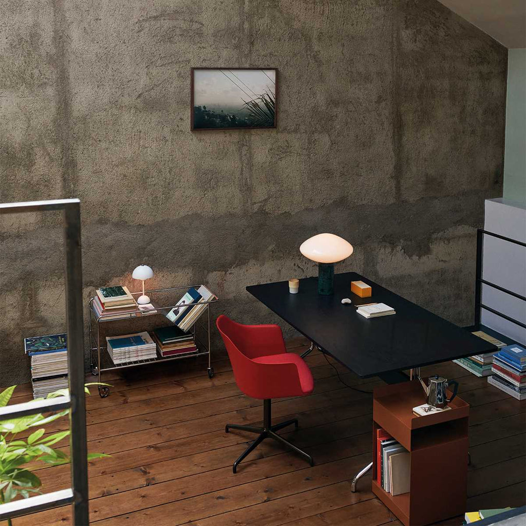 Clérachic table lamp glowing softly on a black desk in the distance, seen across a living space with a red chair.