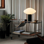 Clérachic marble table lamp lit on a wire bar cart, cropped closer on the potted plant and the cart's top shelf.