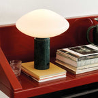 Clérachic marble table lamp on a glossy red shelf, a ribbed glass tumbler and layered magazines set beside it.