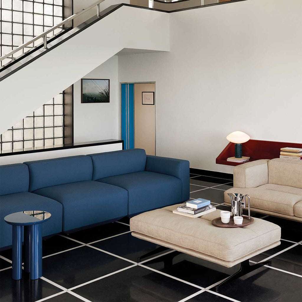 Clérachic marble table lamp on a shelf under a staircase, seen past a blue sofa and cream ottoman in a living room.