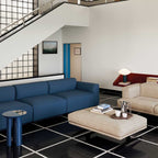 Clérachic marble table lamp on a shelf under a staircase, seen past a blue sofa and cream ottoman in a living room.