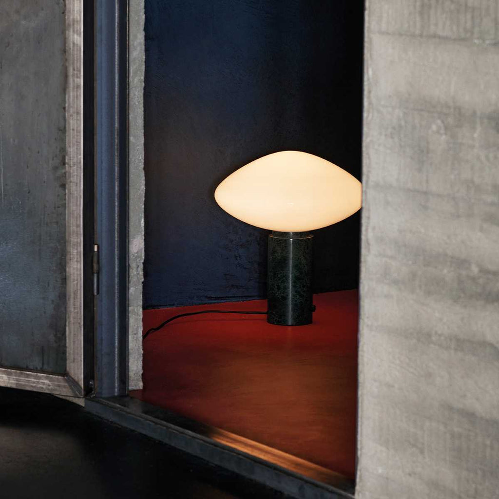Clérachic table lamp lit within a concrete alcove, cropped closer on the lamp against the red floor and blue wall.