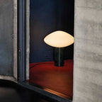 Clérachic table lamp lit within a concrete alcove, cropped closer on the lamp against the red floor and blue wall.