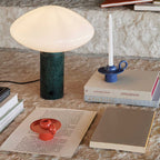 Clérachic table lamp styled on rough stone with a blue candle holder, loose papers and a red saucer beside it.