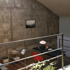 Clérachic marble table lamp lit on a black desk in a loft, seen past a glass balustrade and a red chair below.