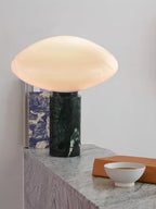 Clérachic table lamp lit on a pale stone ledge beside a blue-patterned book and a small white bowl.