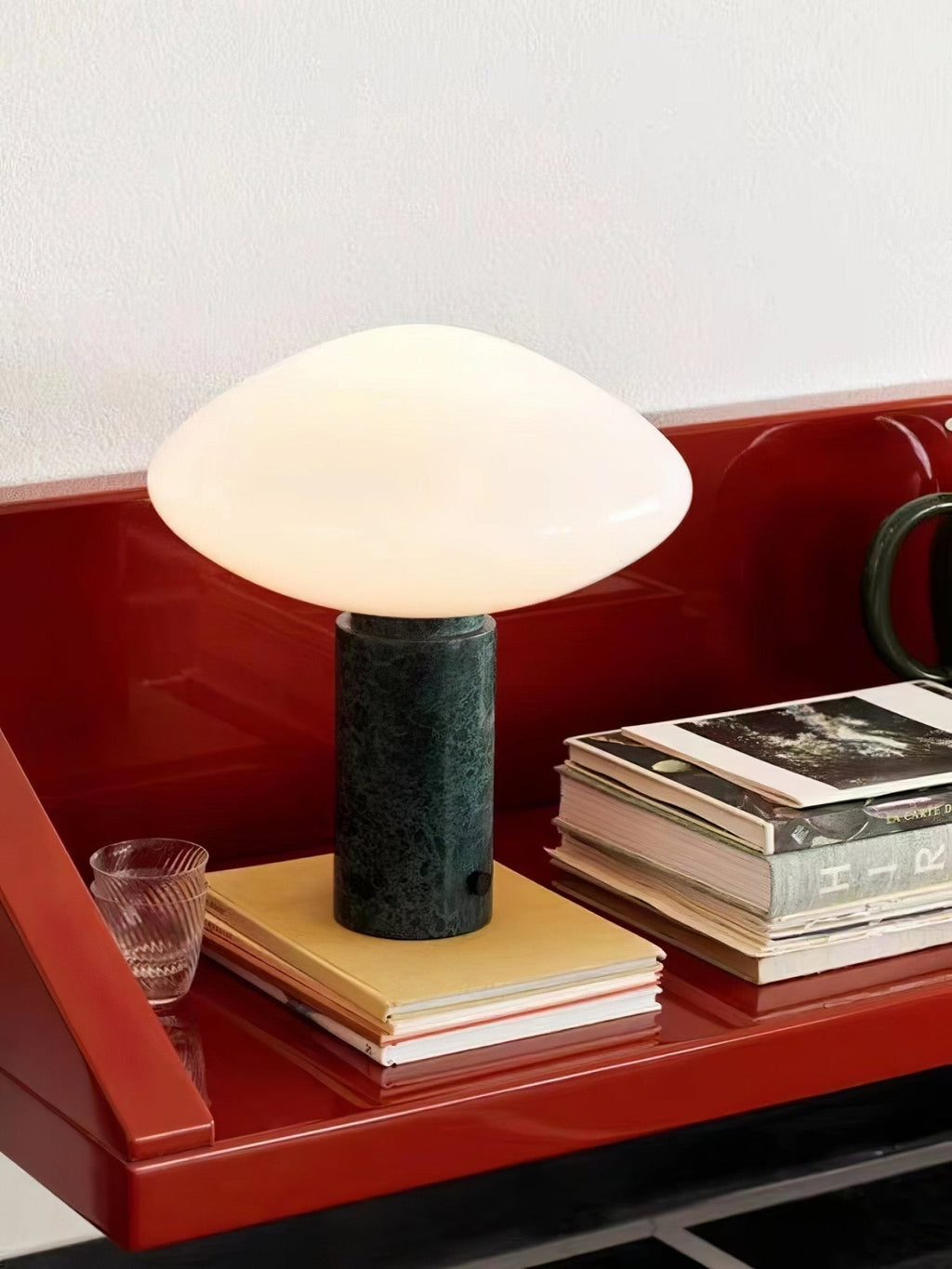 Clérachic marble table lamp on a red lacquered shelf, cropped close on the glass tumbler and stacked books beside it.