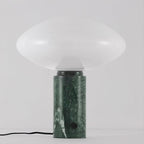 Clérachic green marble table lamp lit against a plain grey background, its veined column and cord shown in full.