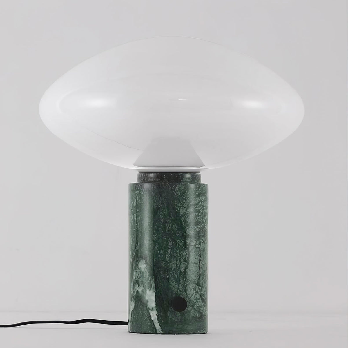 Clérachic green marble table lamp lit against a plain grey background, its veined column and cord shown in full.