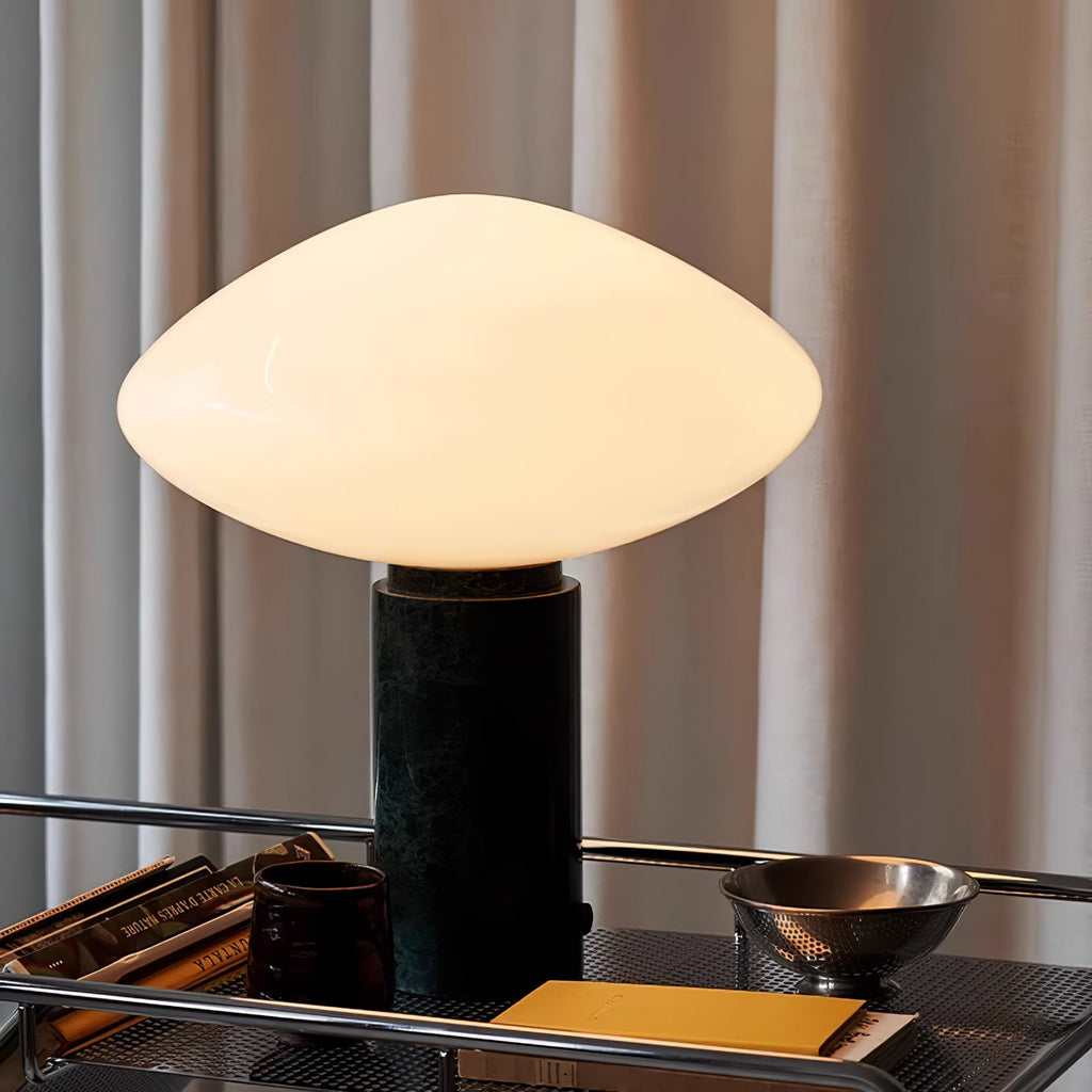 Clérachic marble table lamp lit on a wire-shelf bar cart, curtains behind it and books and a metal bowl close by.