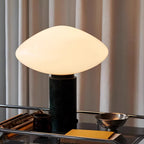 Clérachic marble table lamp lit on a wire-shelf bar cart, curtains behind it and books and a metal bowl close by.