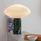 Clérachic table lamp on a pale stone ledge with a patterned blue book, a tan block and a white bowl nearby.