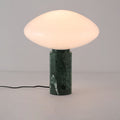 Clérachic green marble table lamp lit against a plain grey background, its veined base and trailing cord in full view.