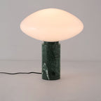 Clérachic green marble table lamp lit against a plain grey background, its veined base and trailing cord in full view.