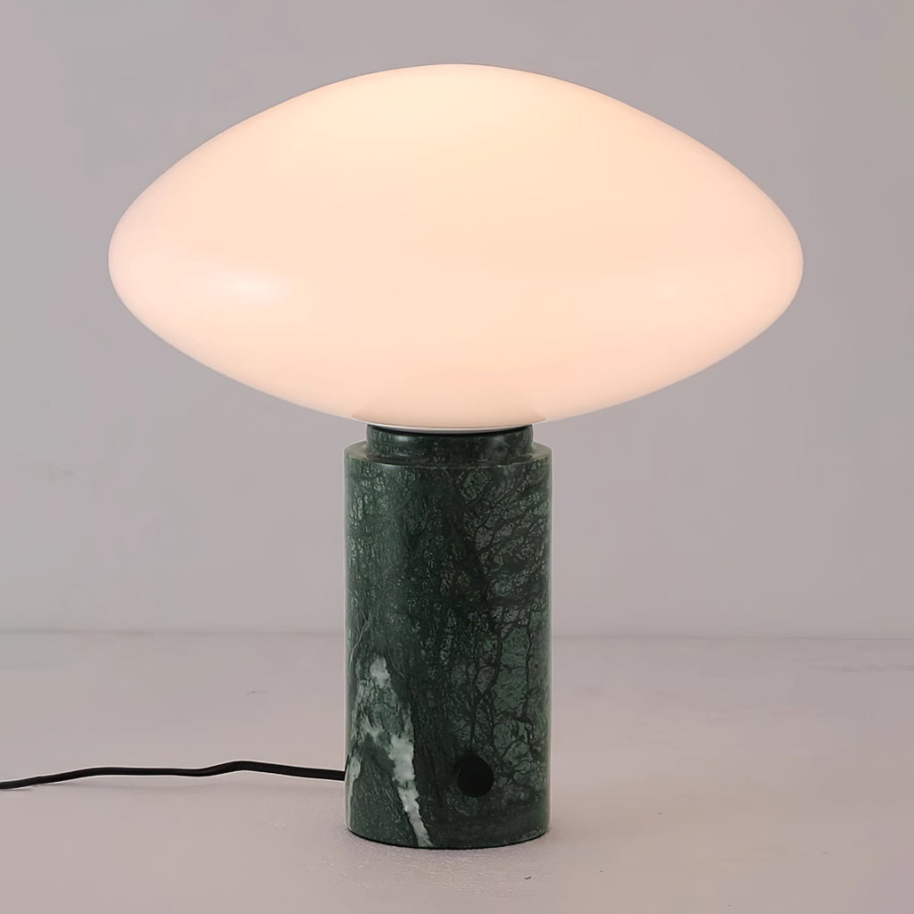 Clérachic green marble table lamp lit against a plain grey background, angled slightly to show the cord looping left.