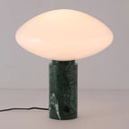 Clérachic green marble table lamp lit against a plain grey background, angled slightly to show the cord looping left.