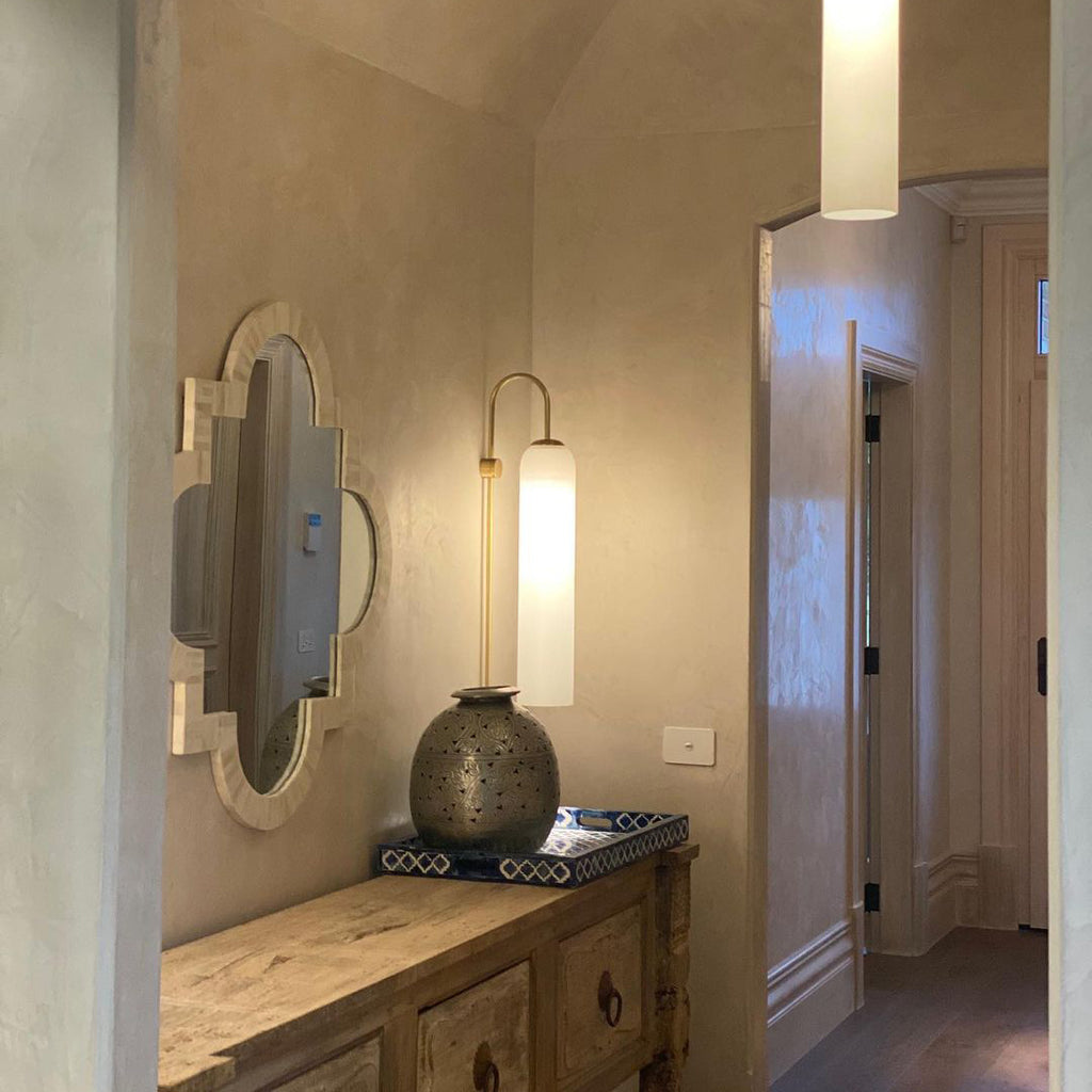 Modern glass wall lamp shown lit beside a mirror