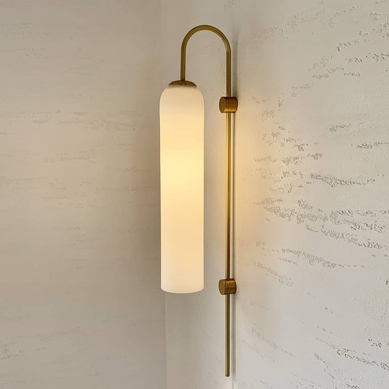 Modern glass wall lamp mounted in a hallway with warm glow