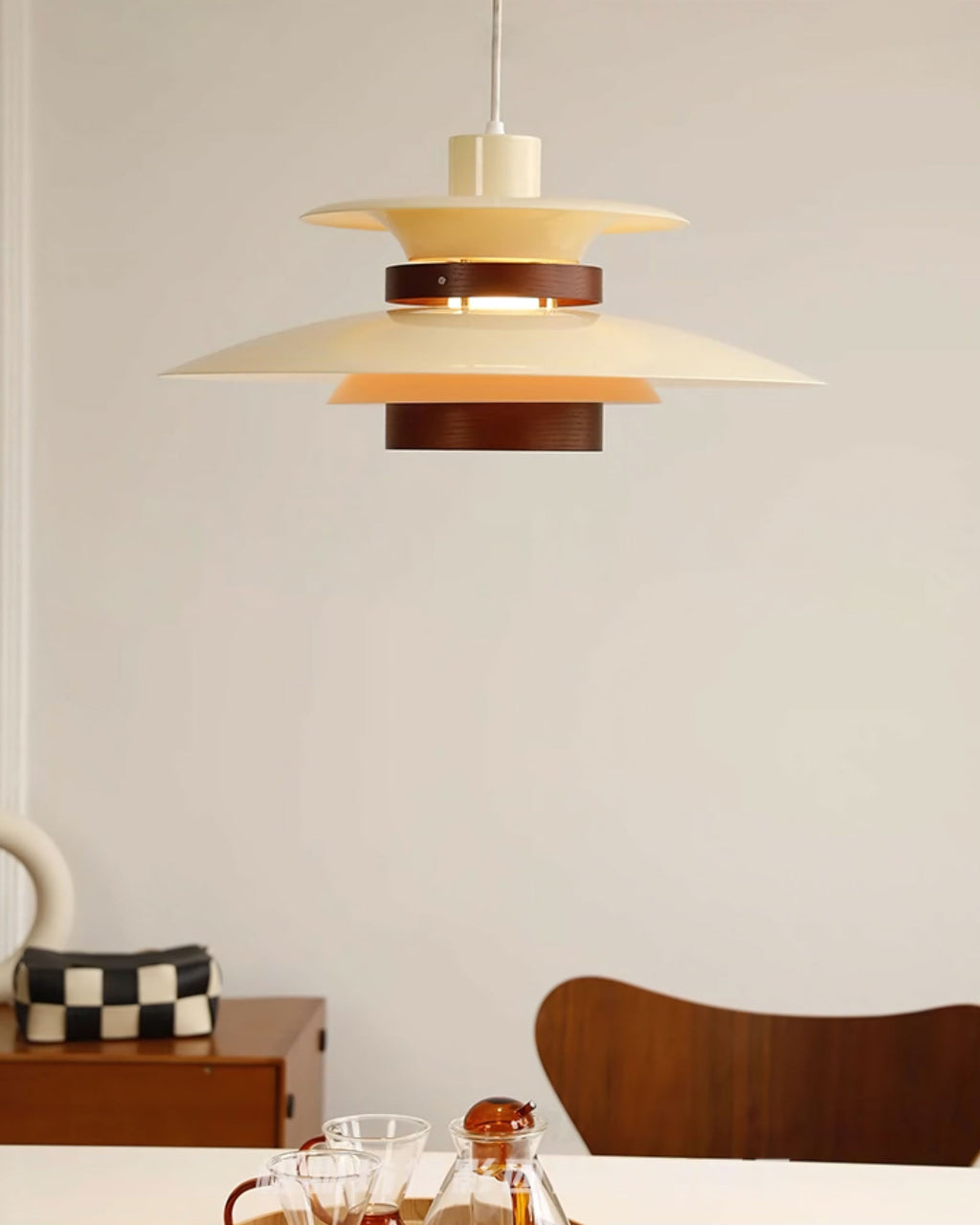 A beige Clérachic pendant hangs near a wooden dining chair and a checked storage box.