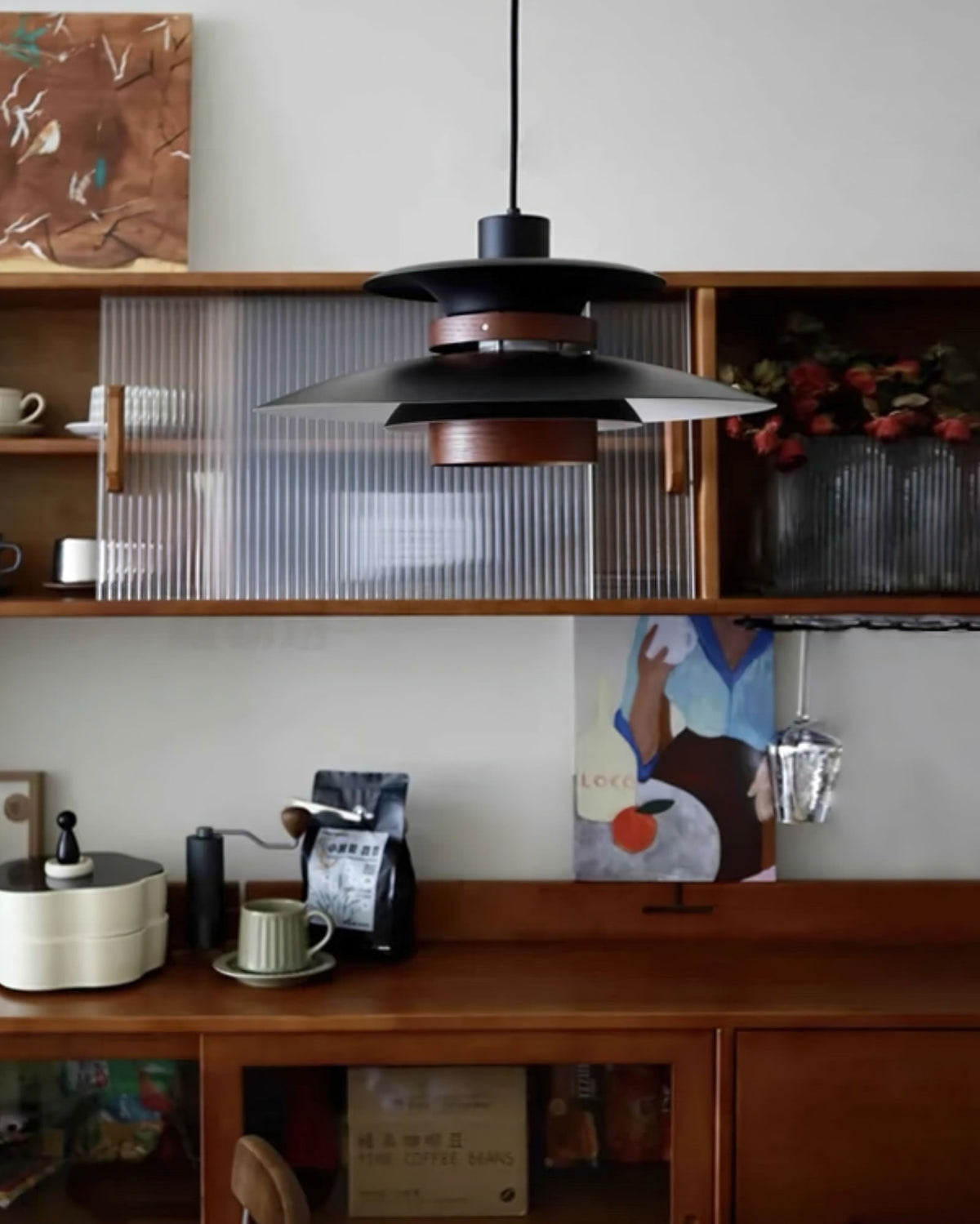 A black Clérachic pendant hangs over open kitchen shelving with mugs and a framed print.
