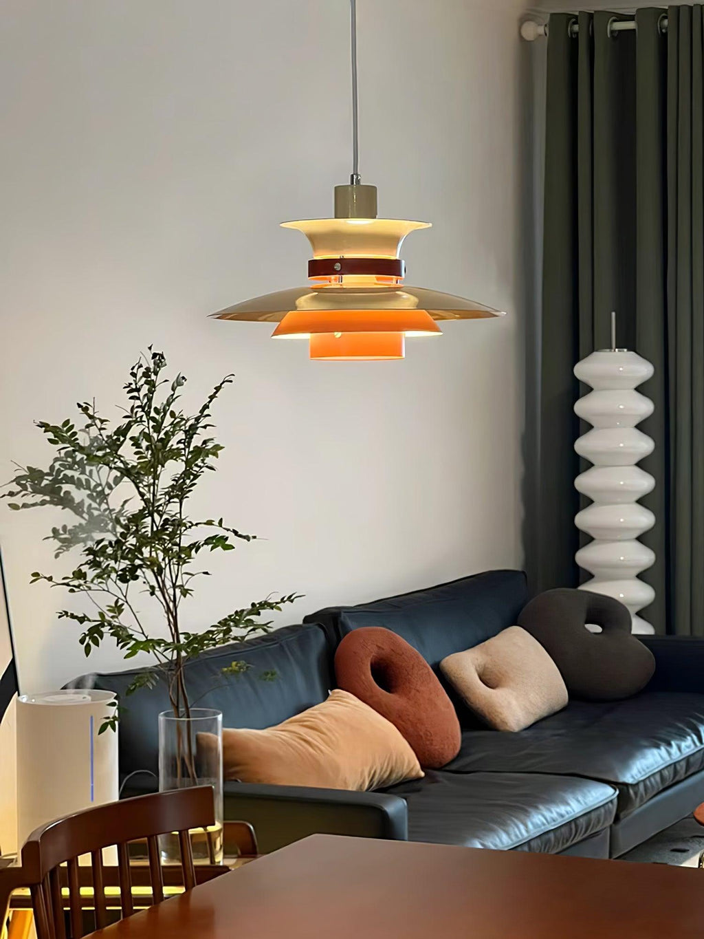 A lit beige Clérachic pendant hangs in a living room with a blue sofa and cushions.