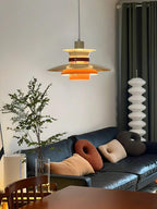 A lit beige Clérachic pendant hangs in a living room with a blue sofa and cushions.