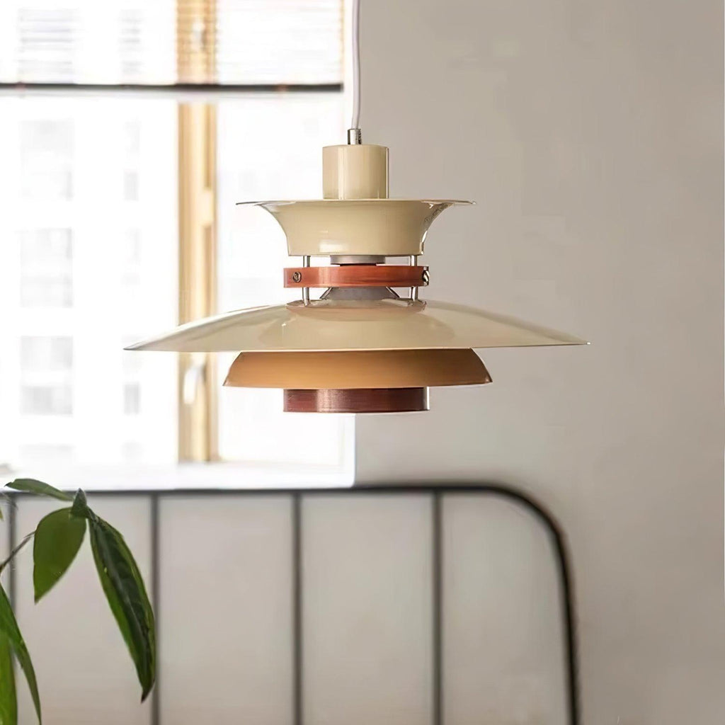 A beige Clérachic pendant hangs near a window with a metal bed frame and plant below.